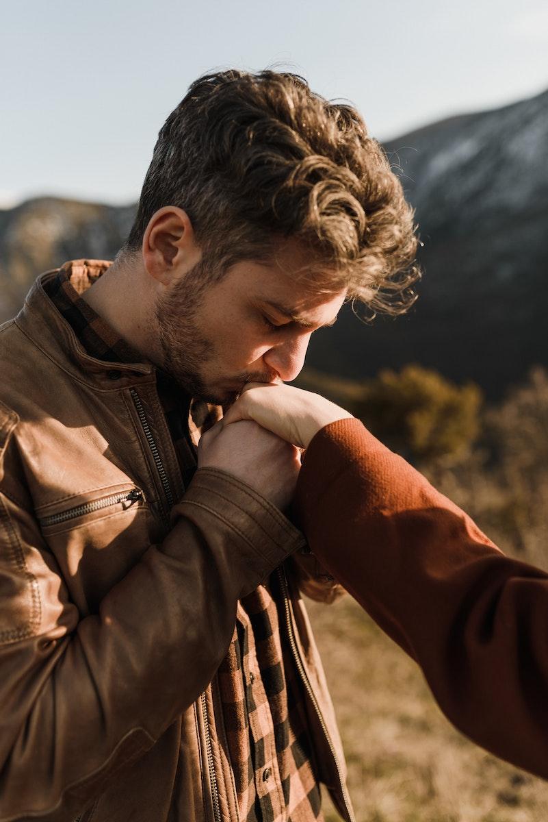 Young man kissing girlfriend hand in hilly sunny nature